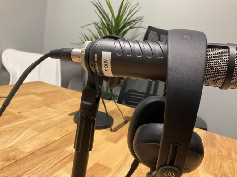Close-up of a microphone on a desk with headphones hanging beside it and a small plant in the background.