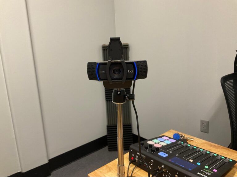 Camera on a tripod beside a lit audio mixer in a small room