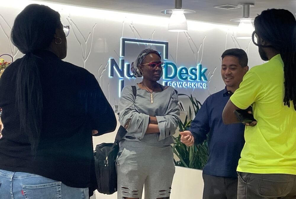 Four people chatting in front of a NiumDesk reception wall in an office lobby.