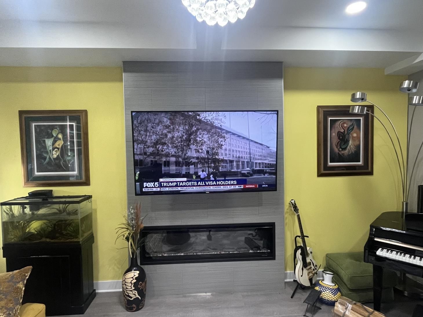 Living room with wall-mounted TV above a fireplace, aquarium left, guitar and piano on the right.