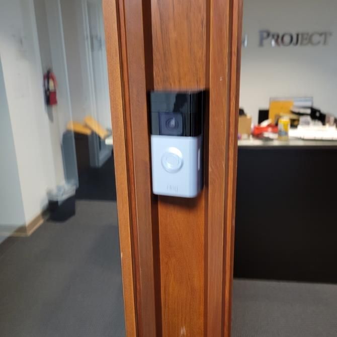 Black intercom or doorbell mounted on a wooden office door frame
