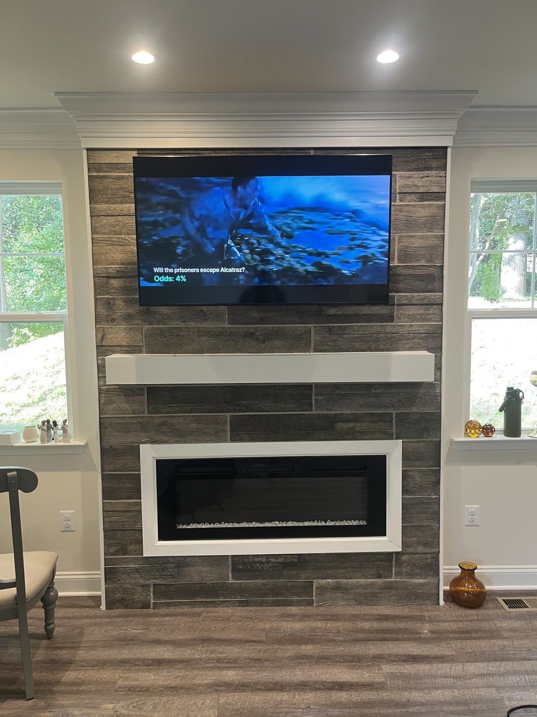 Living room fireplace with mounted TV, stone surround, and windows on both sides