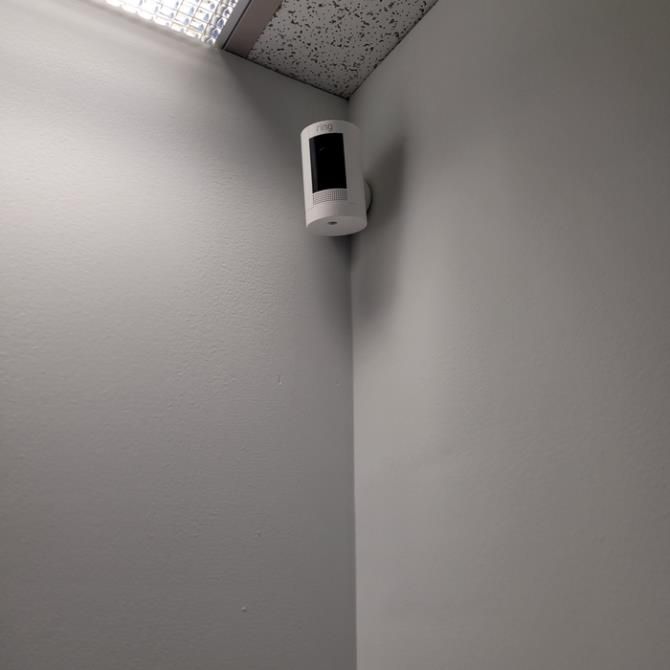 Wall-mounted security camera in a corner near the ceiling, aimed downward.
