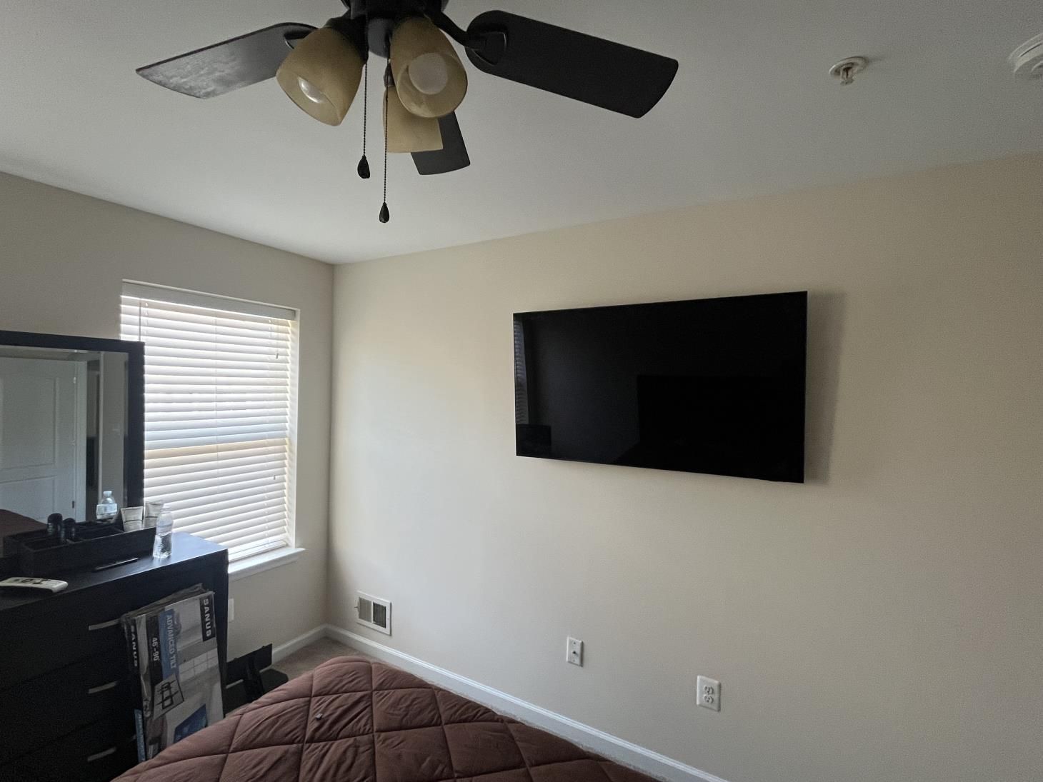 Bedroom with wall-mounted TV, ceiling fan, window blinds, and a bed in the foreground