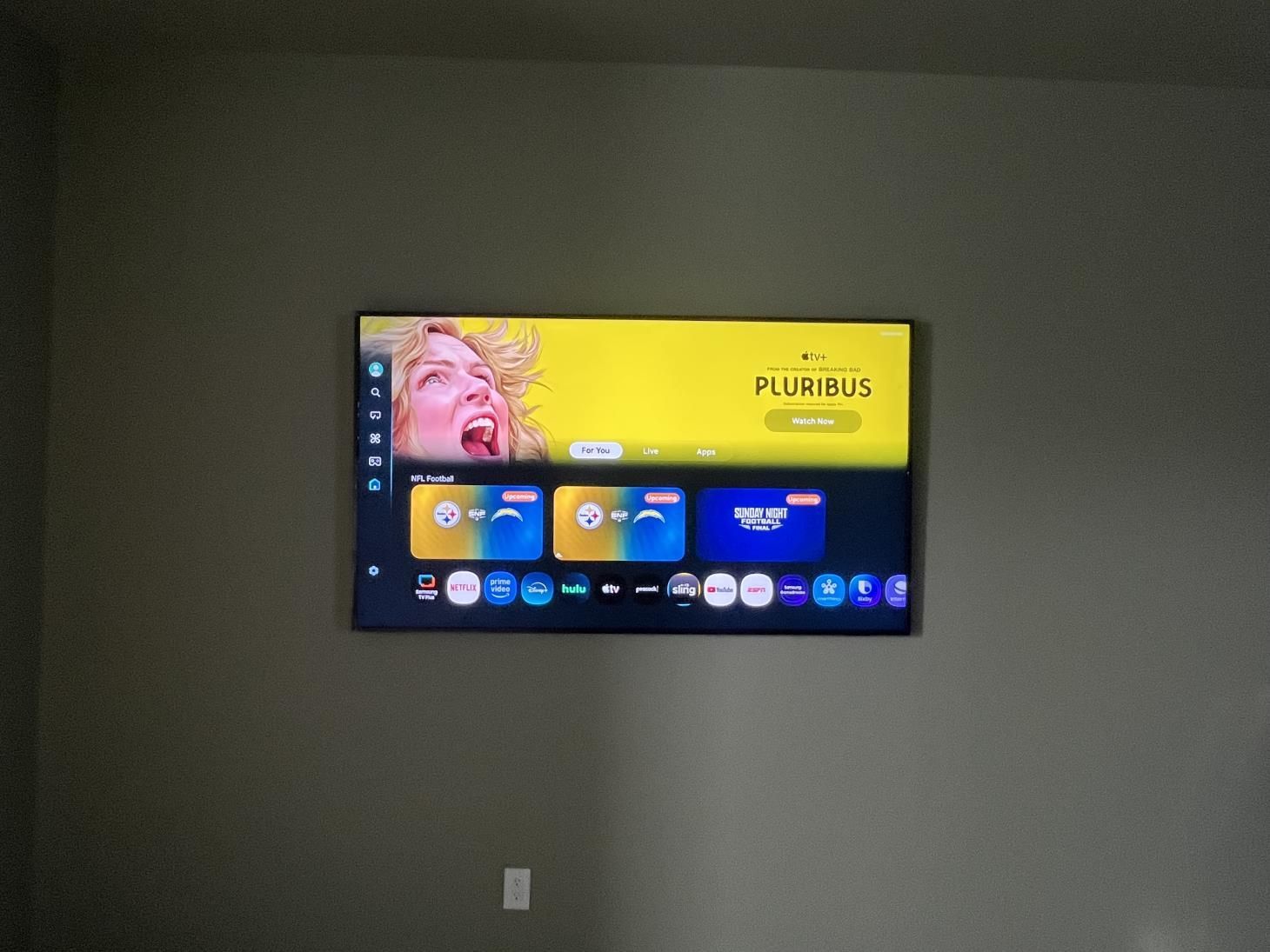 Wall-mounted TV showing a colorful streaming home screen in a plain gray room