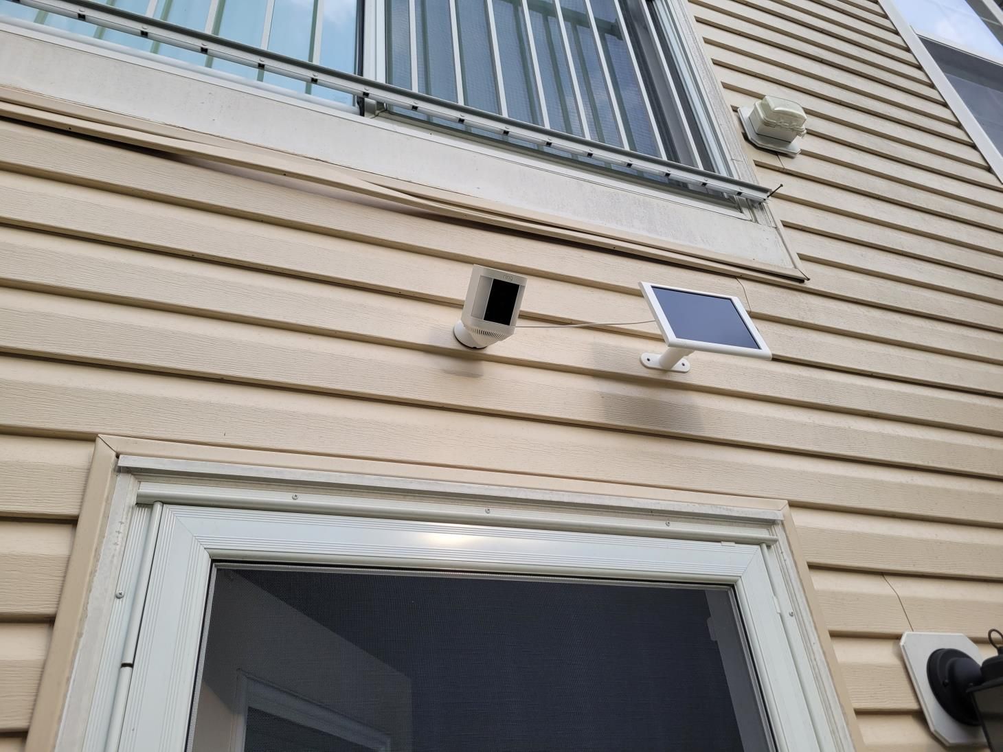 Exterior beige siding wall with a small vent and a solar-powered security light above a window