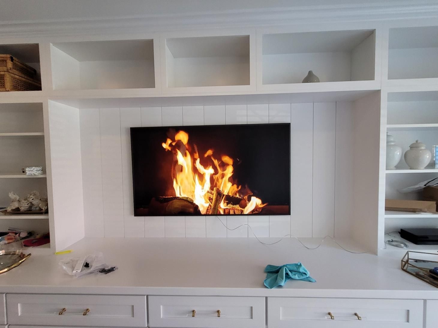 Modern white built-in fireplace with a large fire and empty shelves, with small decor on the sides