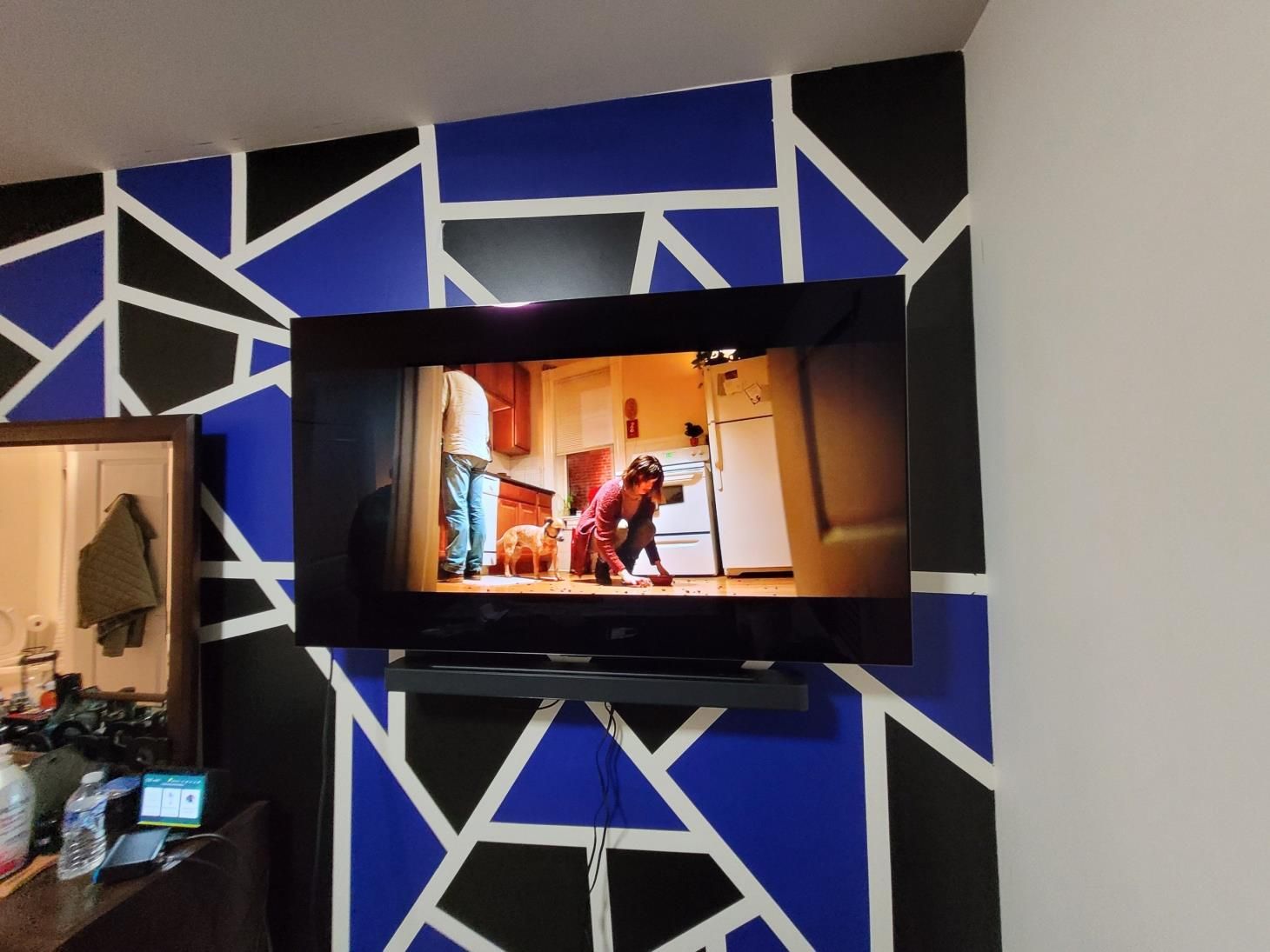 TV mounted on a blue-and-black geometric wall, showing a person in a warm-lit room