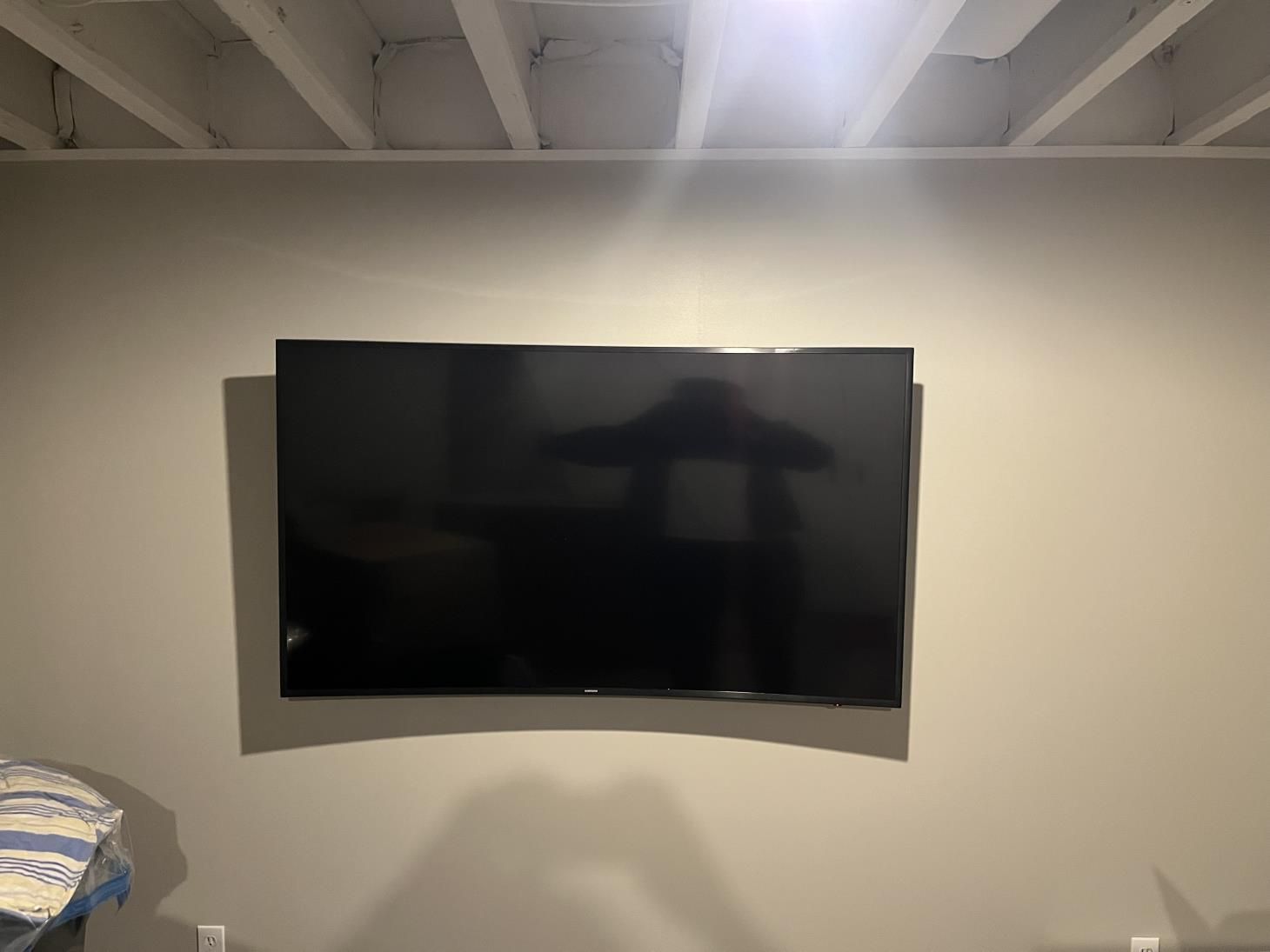 Wall-mounted black TV centered on a beige wall in a room with exposed ceiling beams.