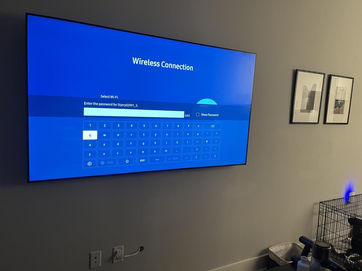 Wall-mounted TV showing Wi‑Fi connection screen in a living room with framed wall art and a chair.