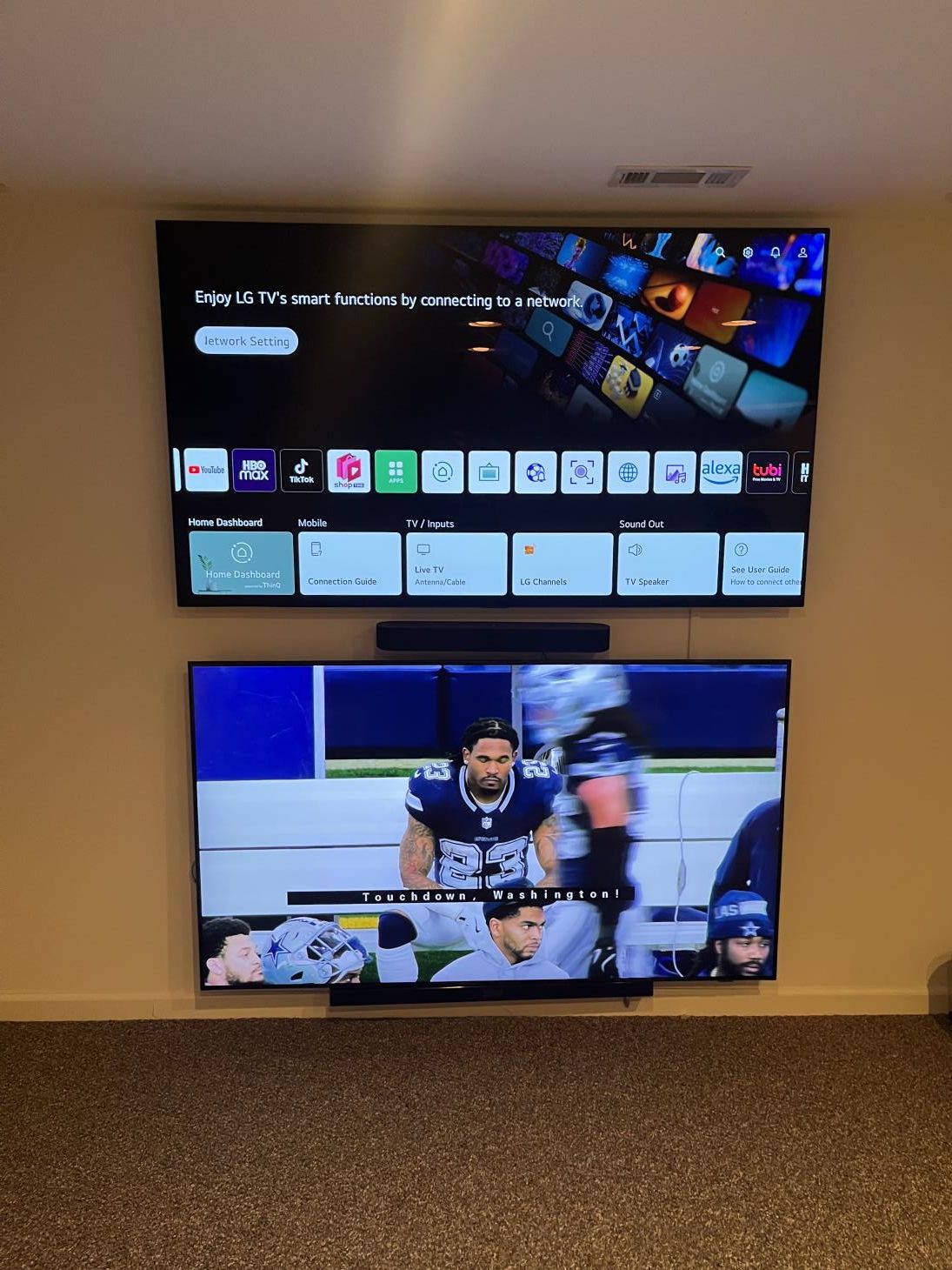 Two wall-mounted TVs, one showing a home screen and the other a football game.