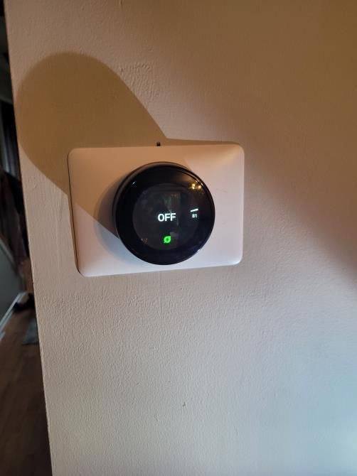 Wall-mounted smart thermostat with a black round display showing “OFF” on a beige wall.