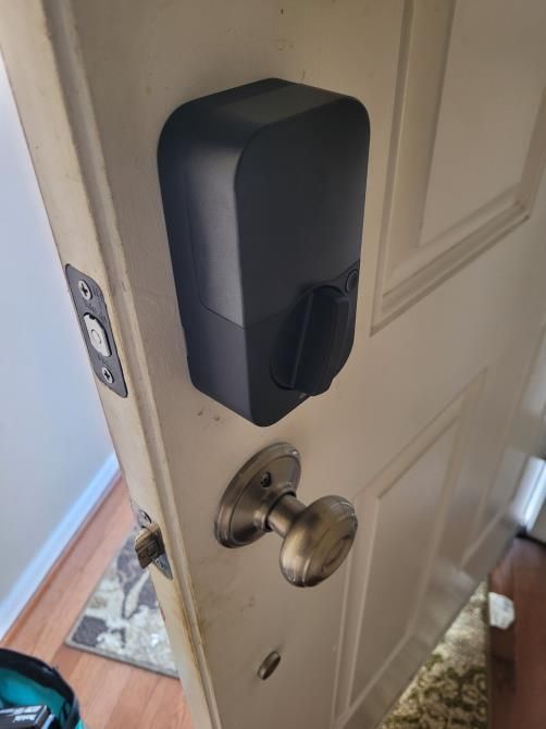 Door with black smart lock and silver knob partially open near a doorway.