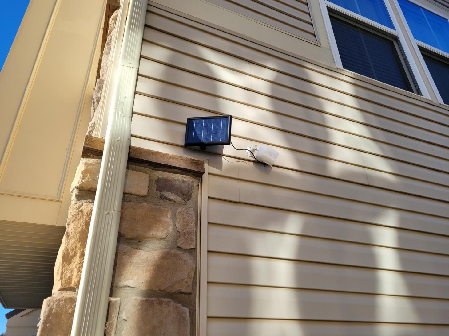Blue wall-mounted light on beige siding beside a stone corner and window on a house exterior