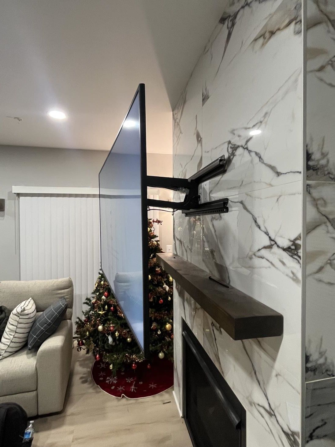Living room with a wall-mounted TV, marble fireplace, and small decorated Christmas tree