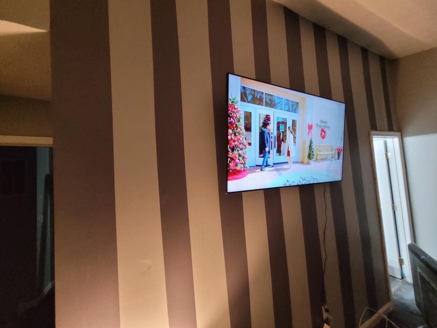 TV mounted on a striped wall in a bright room, with a window and furniture nearby