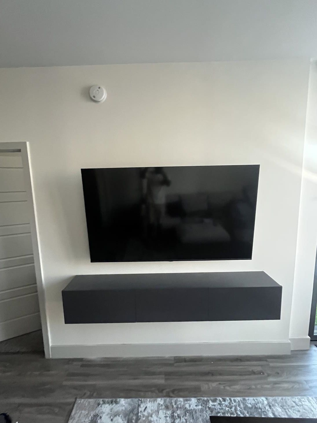 Wall-mounted TV above a floating black media console on a white wall in a modern room