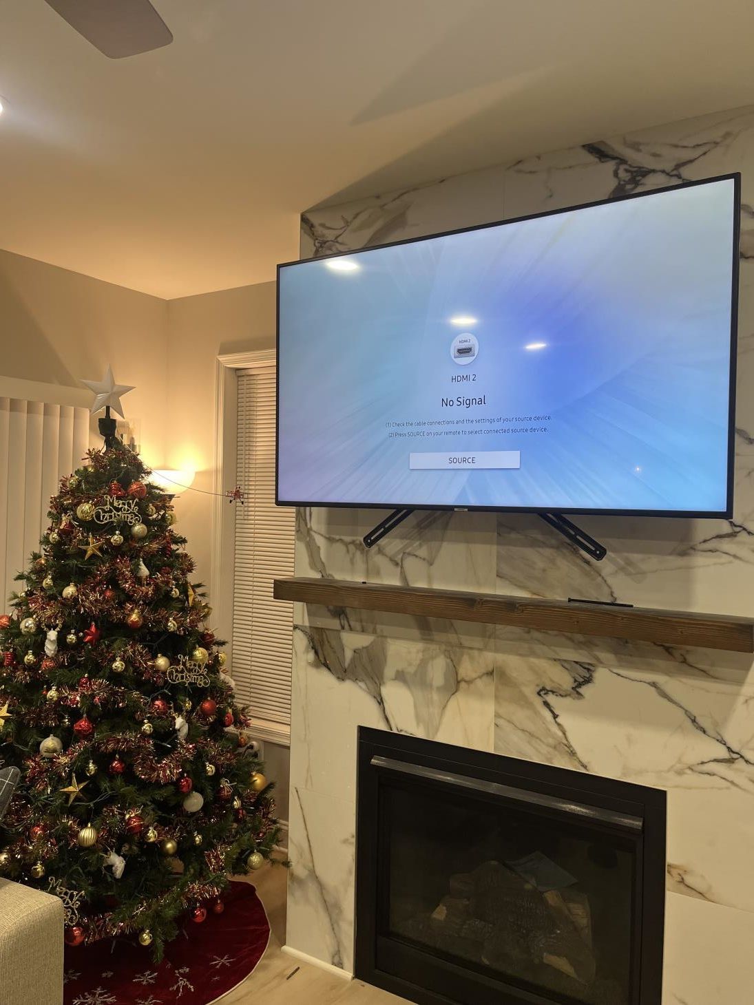 Living room with a decorated Christmas tree beside a TV mounted above a fireplace