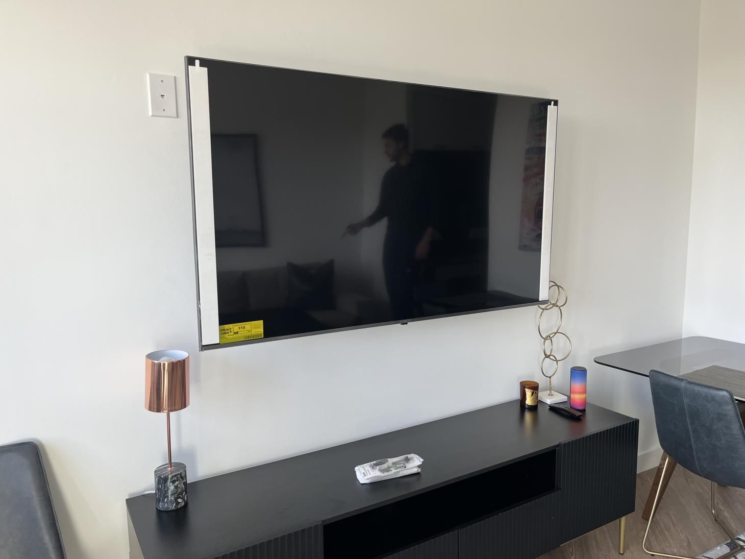 Wall-mounted TV above a black console in a modern living room with a lamp and chair nearby.
