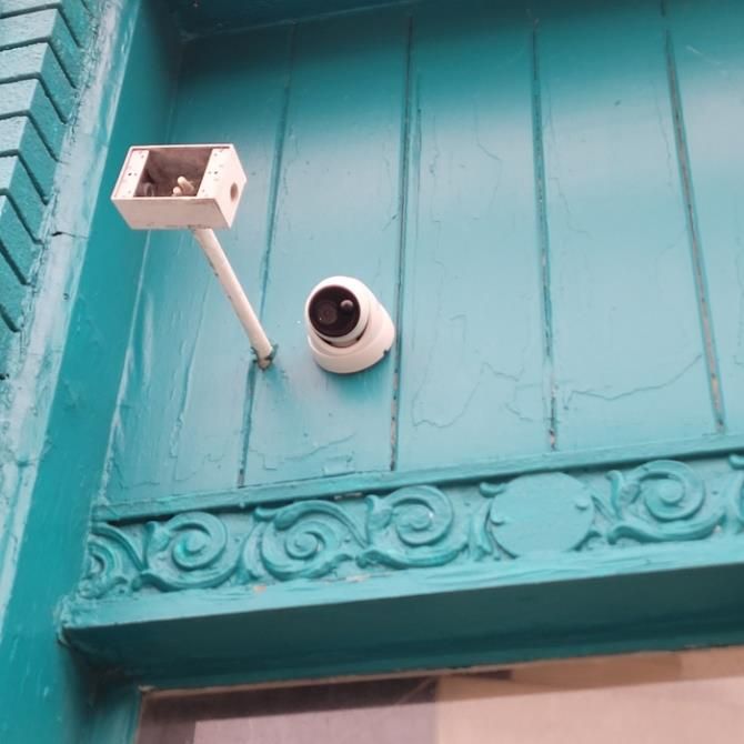 White security camera and small light mounted on a turquoise wall above decorative trim