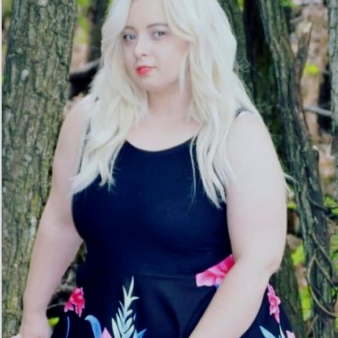 A woman in a black dress is standing in front of a tree