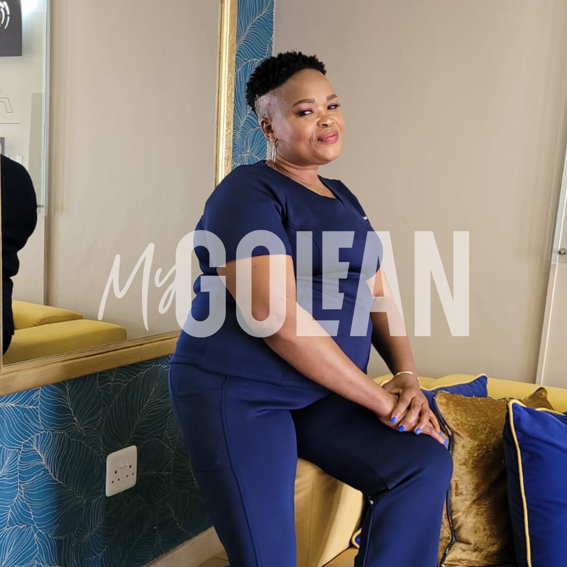 A woman in a blue outfit is sitting on a couch in front of a mirror.