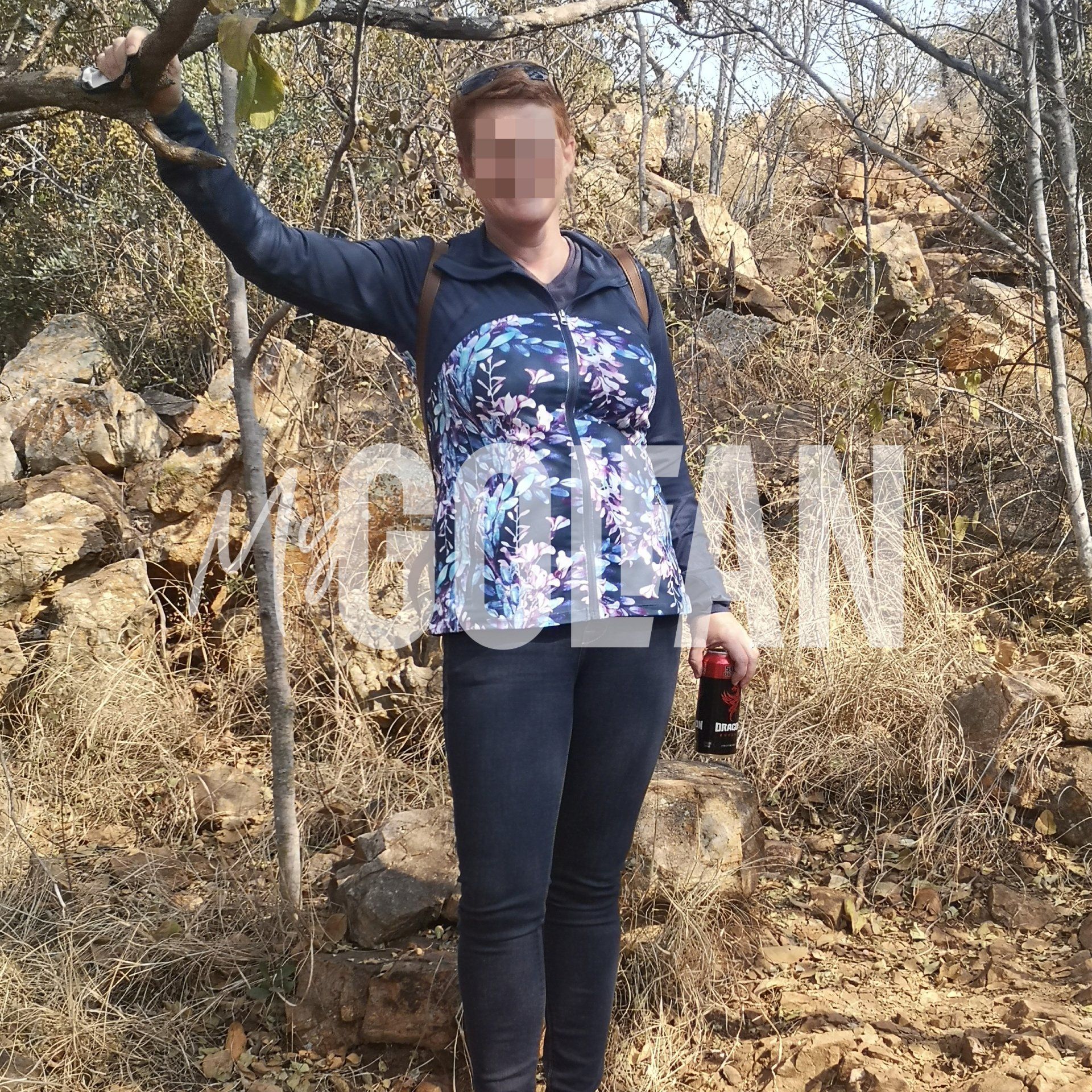 A woman in a floral shirt is standing in the woods