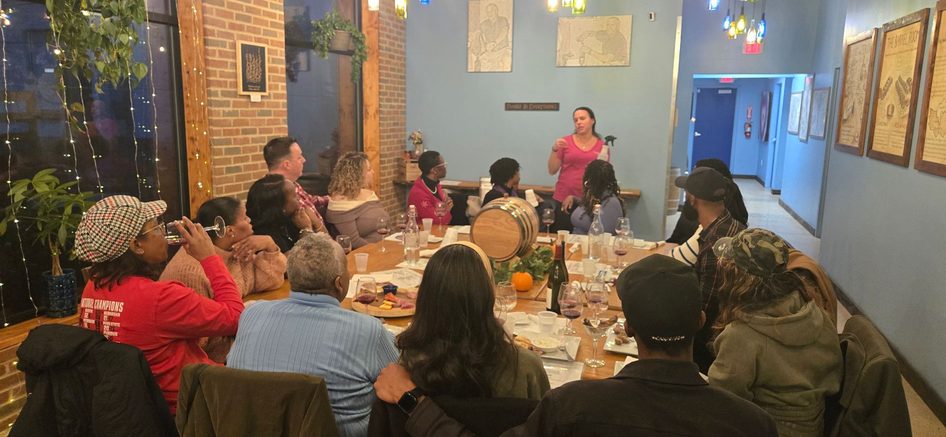 People seated around a table in a cozy restaurant or café, listening to a speaker near a brick wall