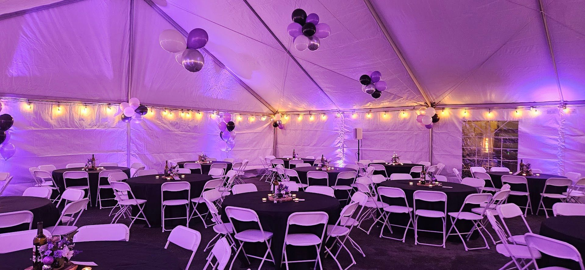 Purple-lit event tent with rows of white chairs and round tables set for a gathering