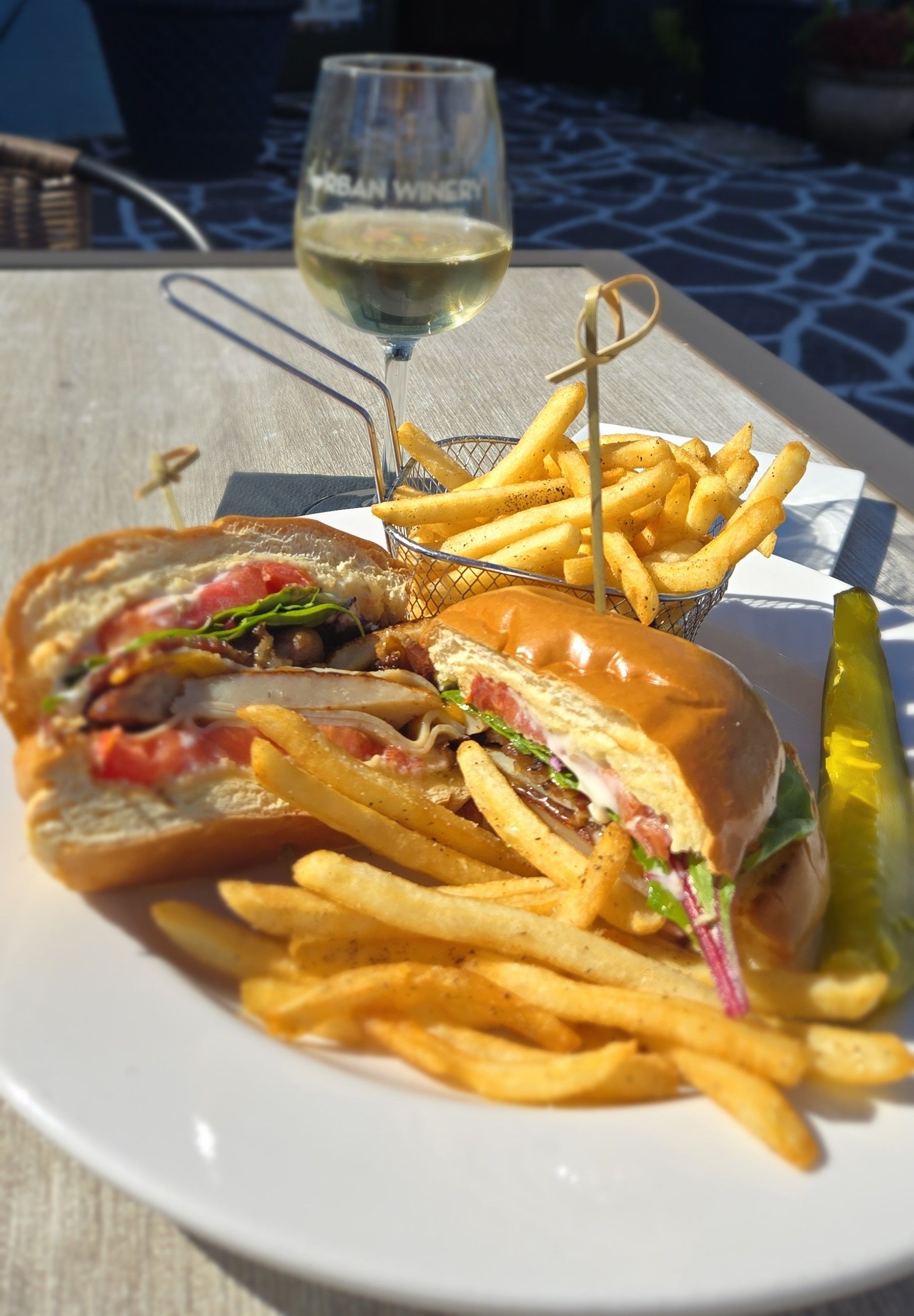 Sandwich and fries on a white plate with a glass of white wine outdoors