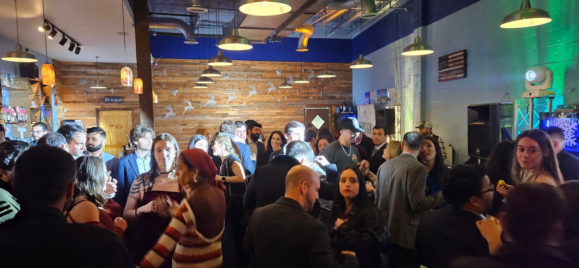 Crowded indoor bar with people socializing under warm lights and a brick wall backdrop