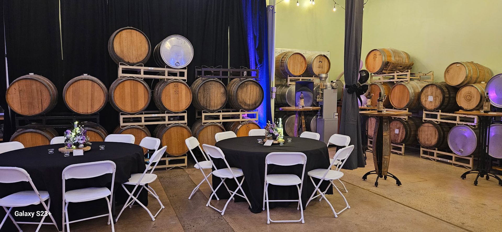 Wine barrel-lined event space with white folding chairs and tables set up in the foreground