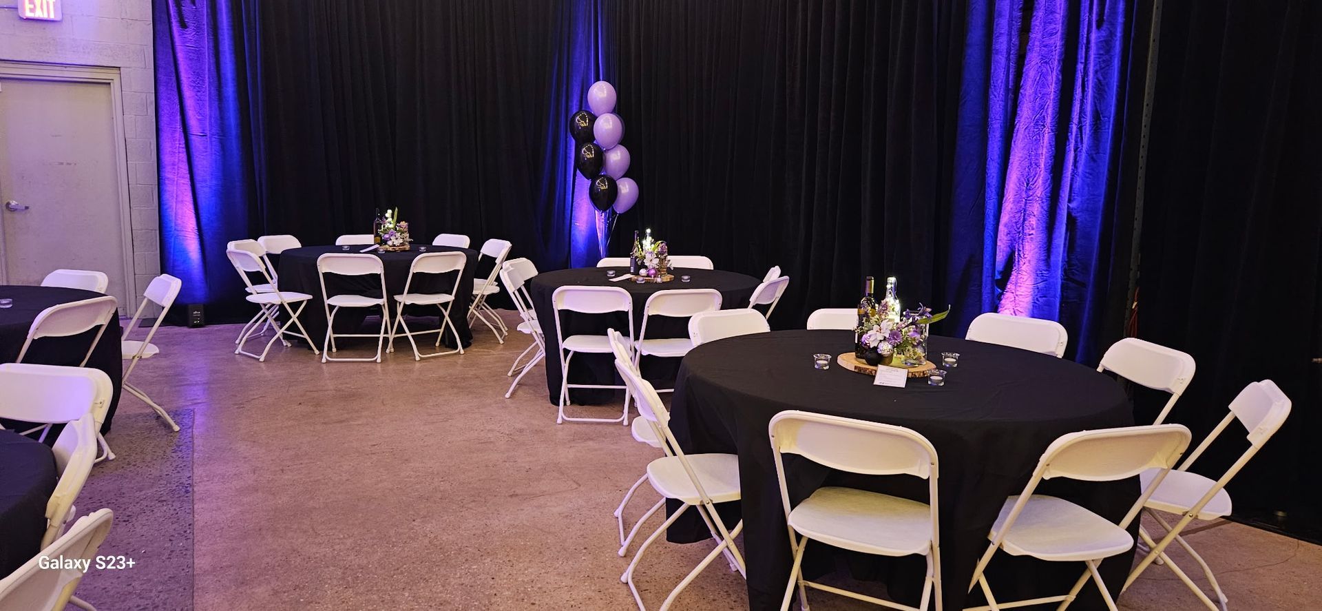 Banquet hall with round tables, white folding chairs, and purple-lit curtains