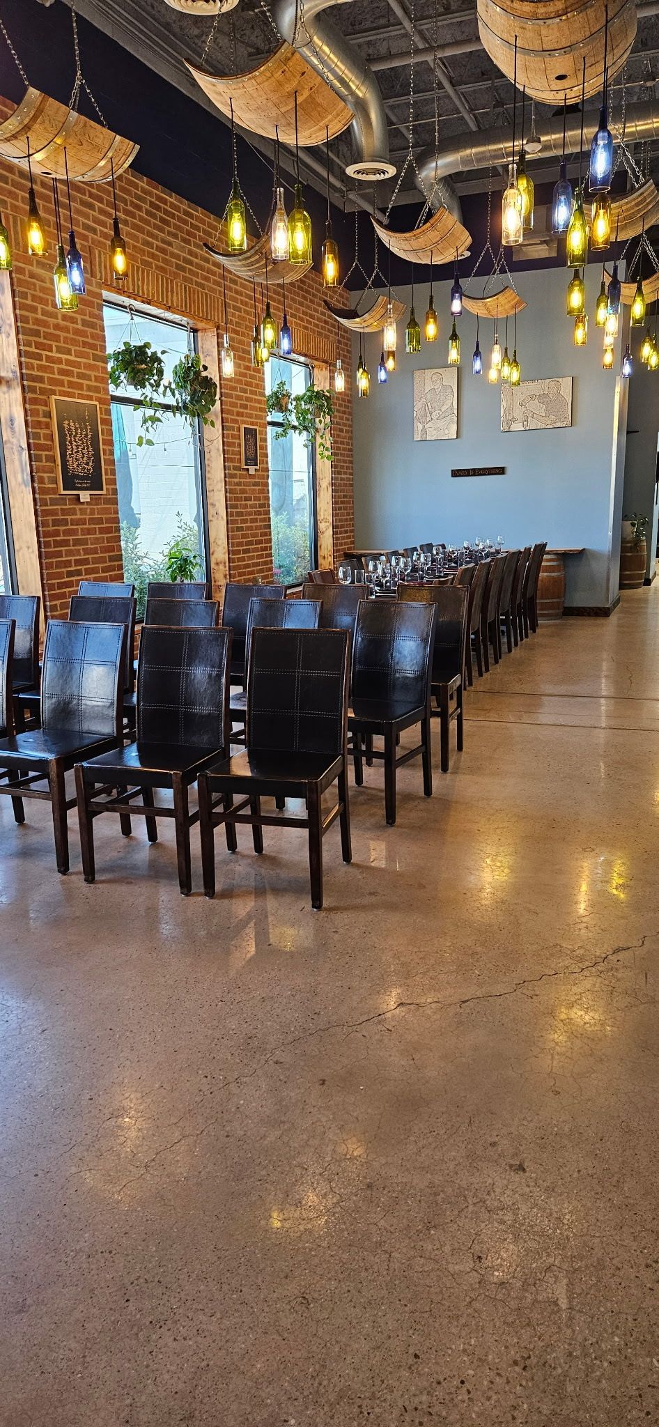 Empty modern restaurant with rows of black chairs, hanging lights, and large windows by a polished floor
