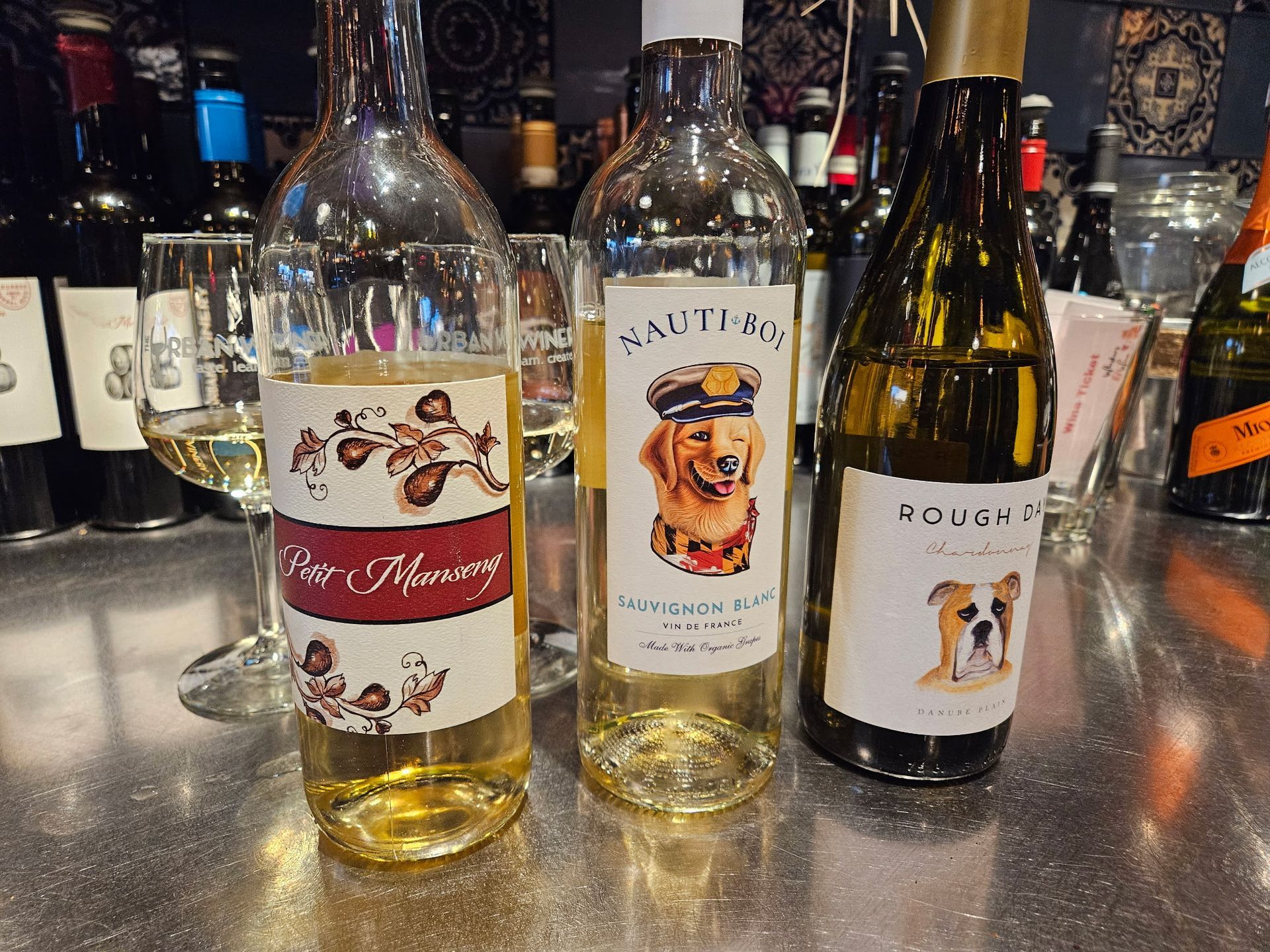 Three wine bottles on a bar counter, including two white-label bottles and one dark bottle with dog labels.