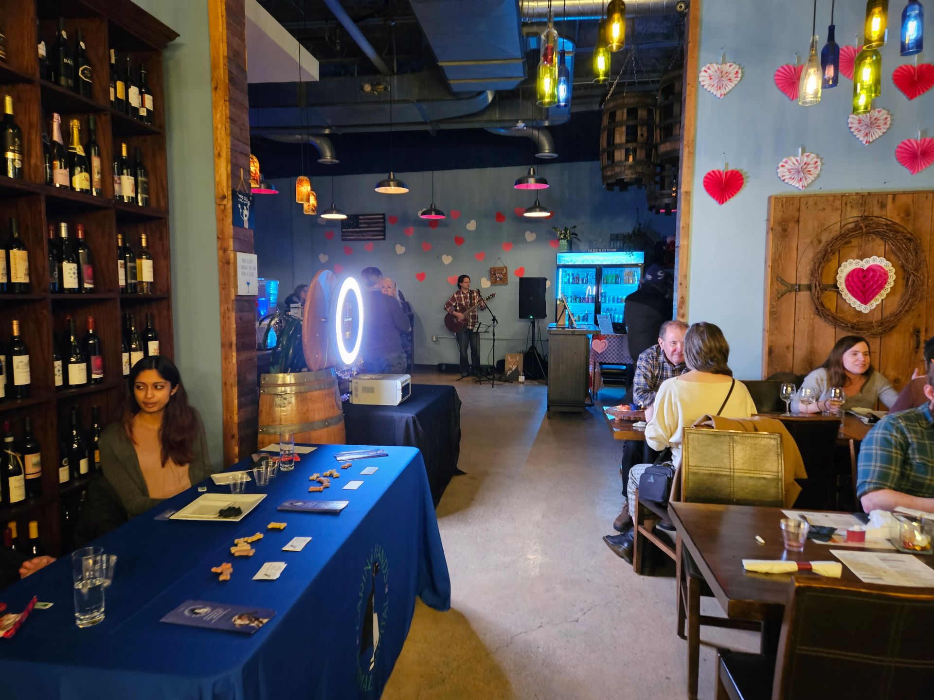 Cozy restaurant interior with blue tablecloths, hanging lanterns, red heart decorations, and seated diners.