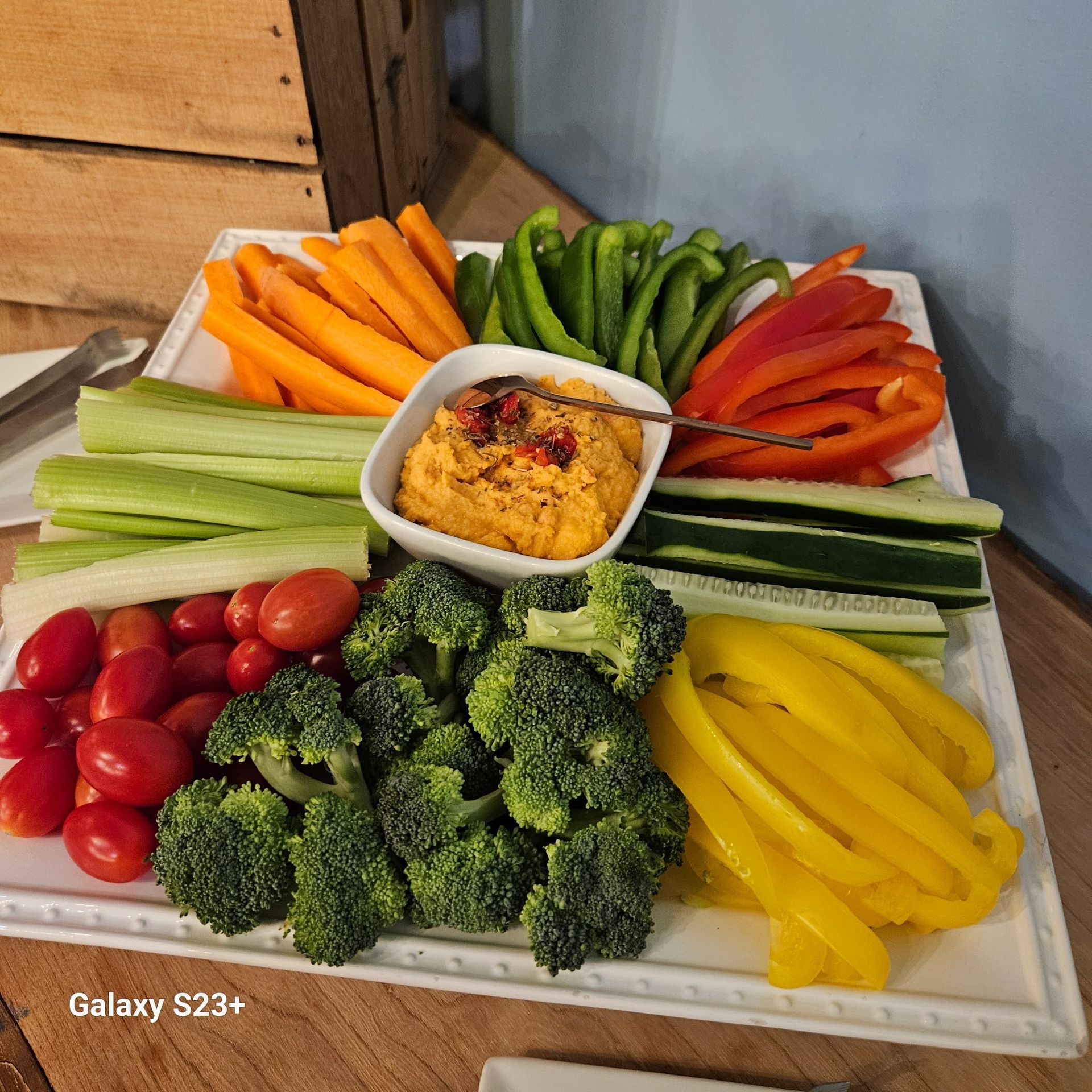 Fresh vegetable platter with celery, carrots, cucumbers, peppers, broccoli, tomatoes, and a dip in the center