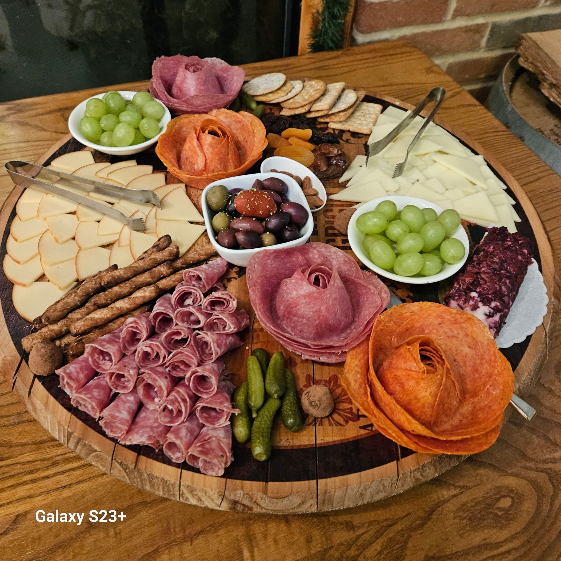 Charcuterie board with assorted cheeses, meats, grapes, crackers, and dips on a round wooden table