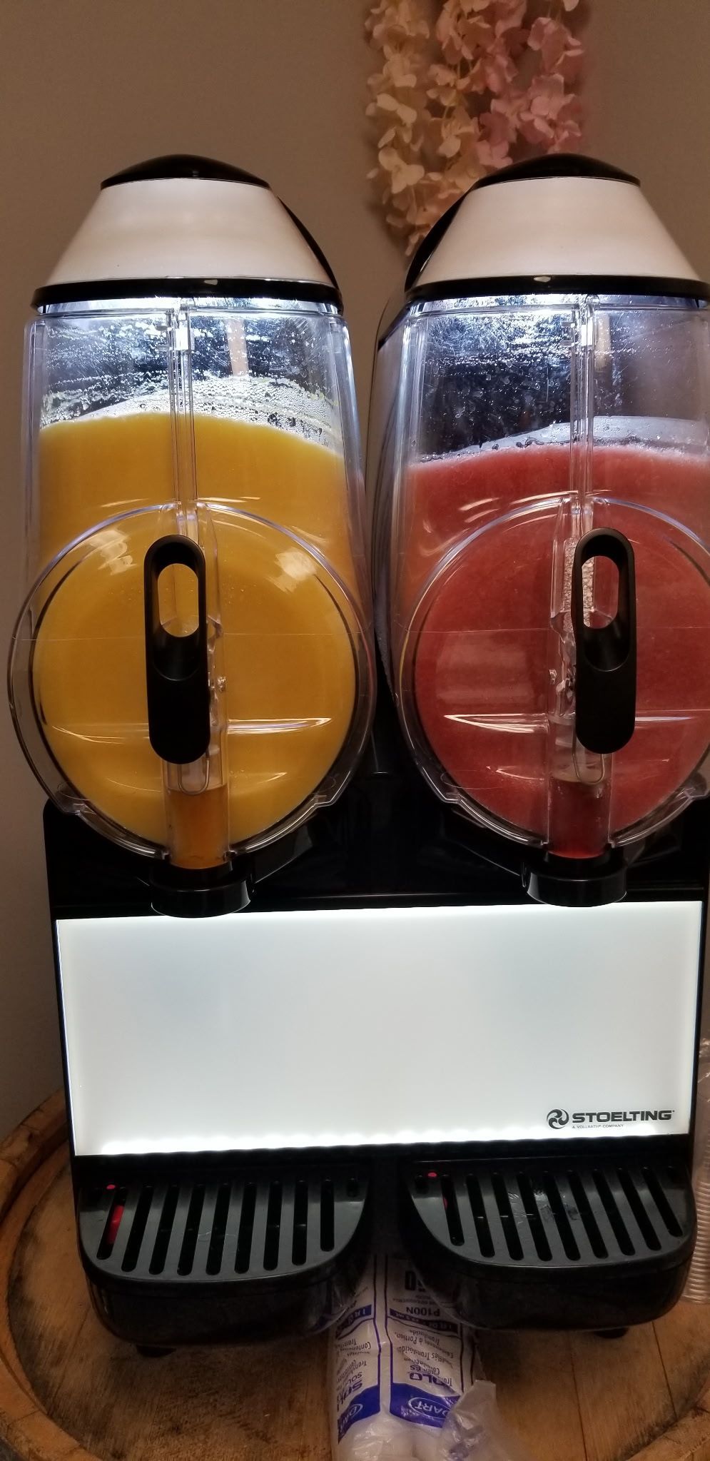 Two colorful liquid dispensers with black bases, orange on the left and red on the right, on a white counter