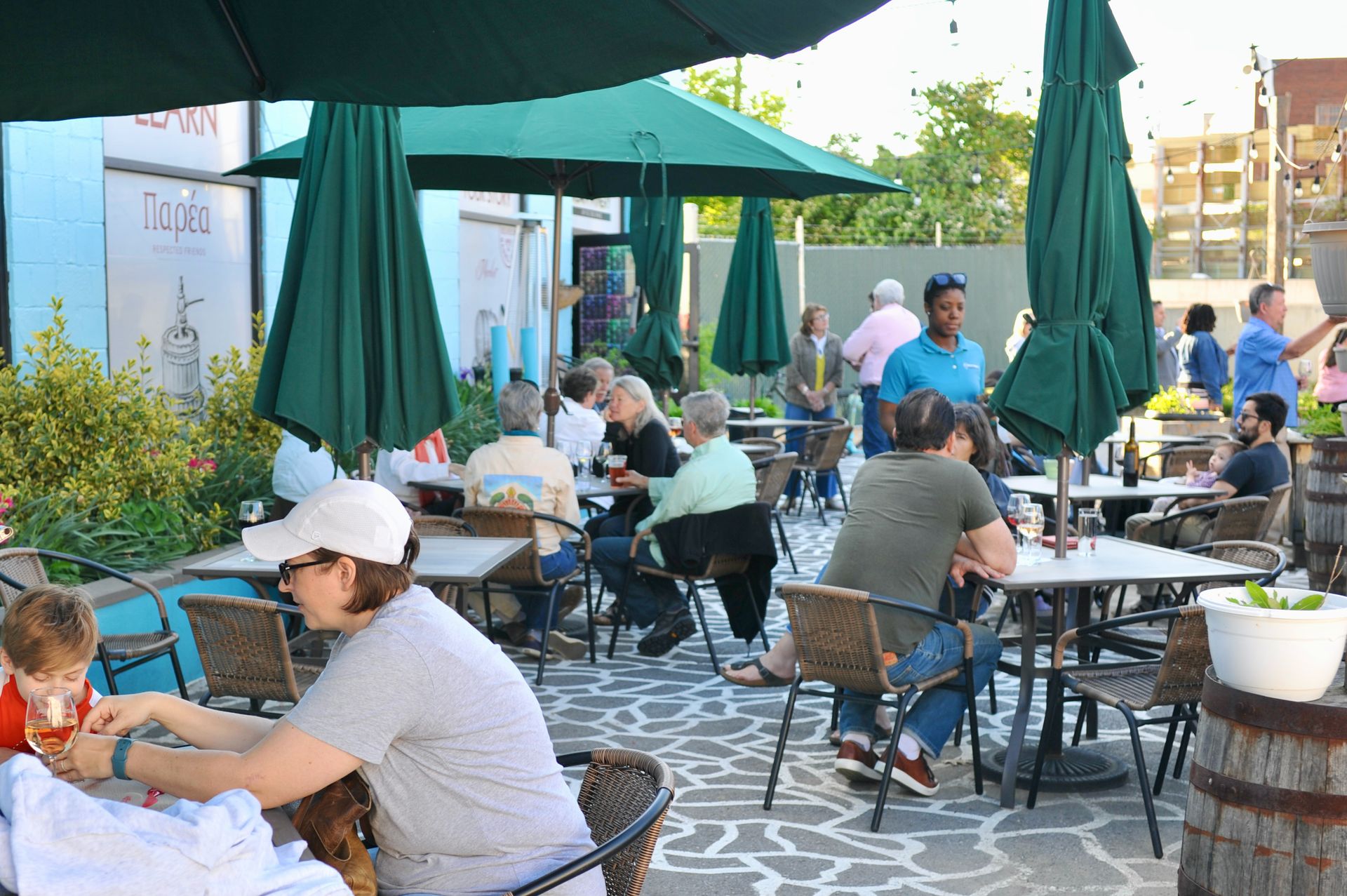 Outdoor café with people seated at tables under green umbrellas on a sunny patio
