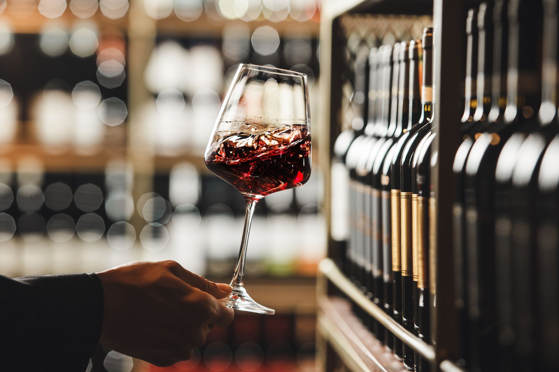 A person is holding a glass of red wine in a wine cellar.