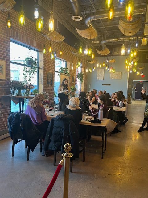 People seated at tables in a warmly lit restaurant with hanging pendant lights and a red velvet rope barrier