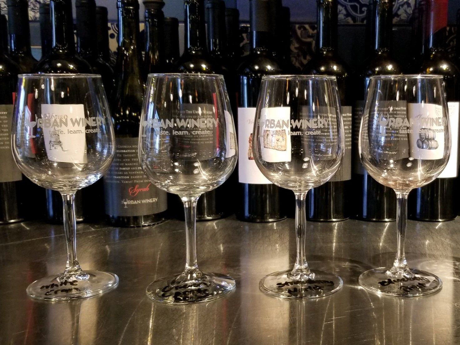 Four empty wine glasses on a table in front of dark wine bottles