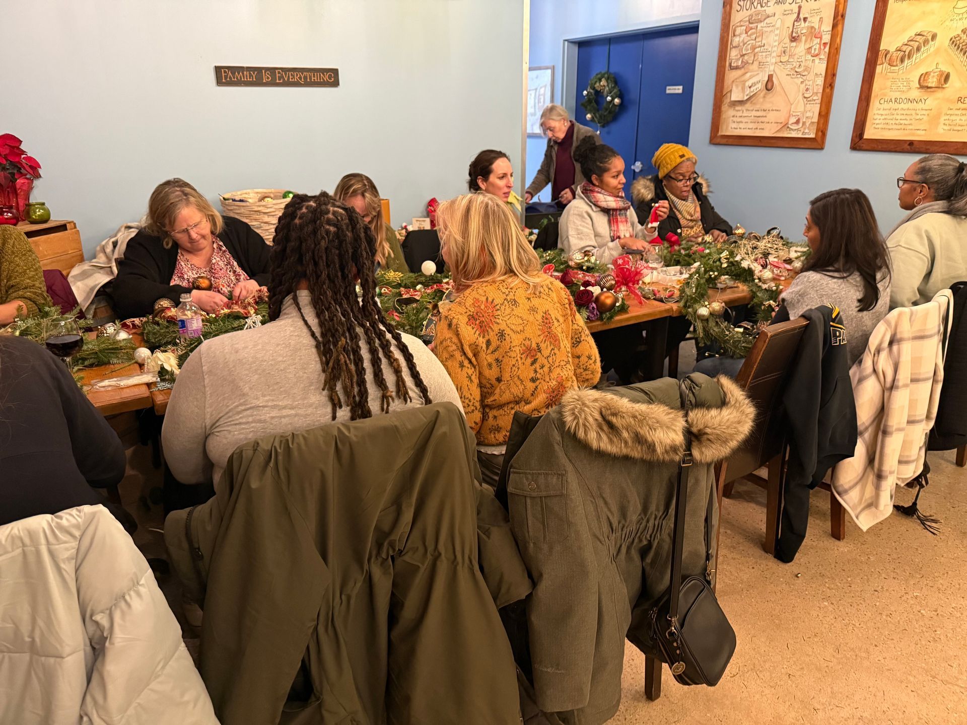 People seated around a long dining table in a cozy room, sharing a meal with coats hanging on chair backs.