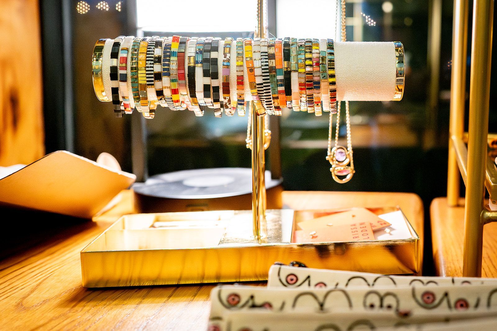 Colorful beaded cylindrical display on a stand, lit warmly on a tabletop in a shop or gallery.