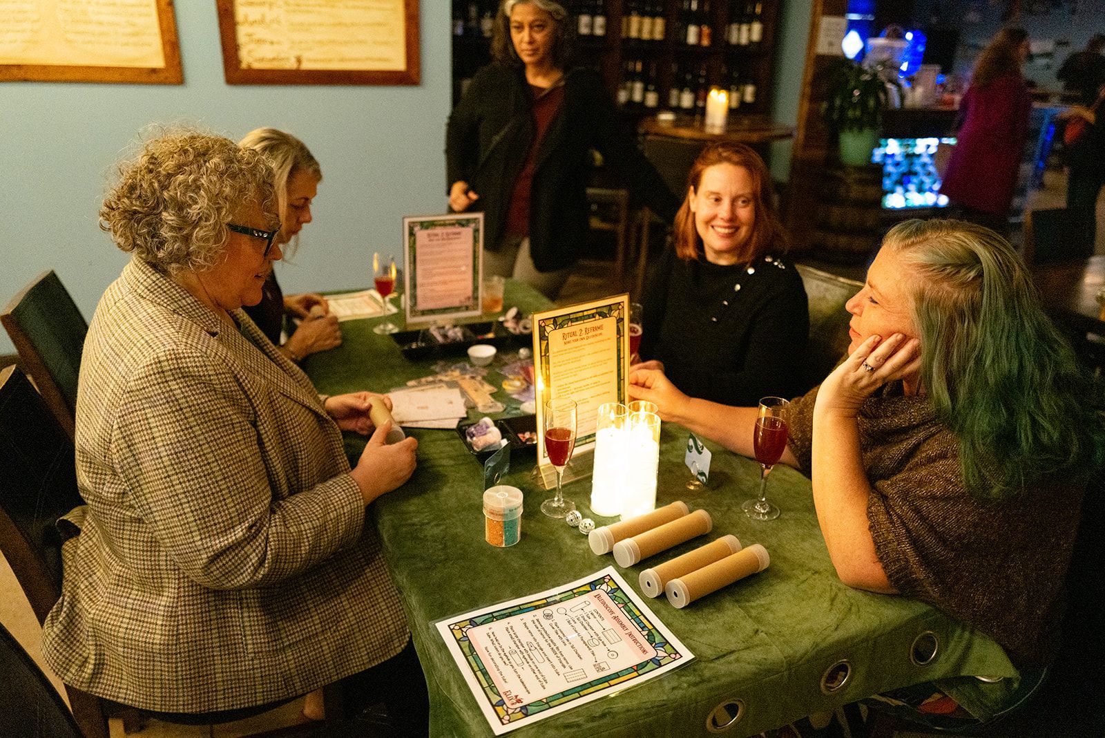 Three people sit at a small table in a cozy café, talking over drinks and menus.