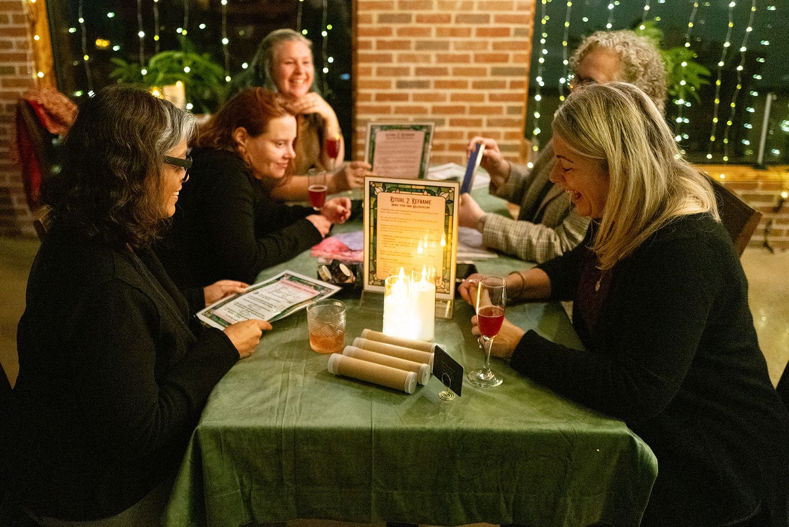 People seated around a candlelit table at a restaurant, chatting and holding drinks.