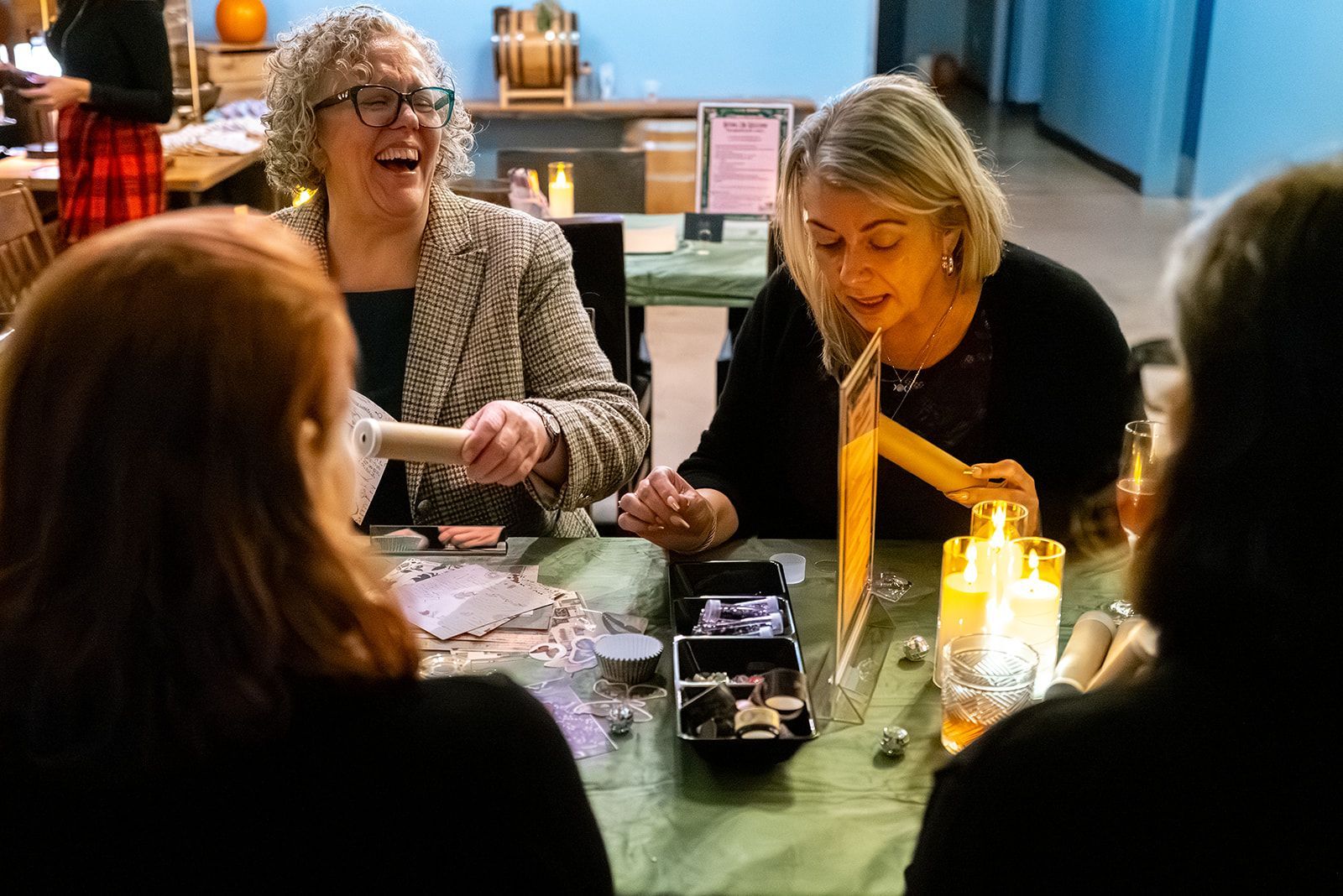 People gathered around a table with papers and a lit candle, smiling and talking in a warm indoor setting