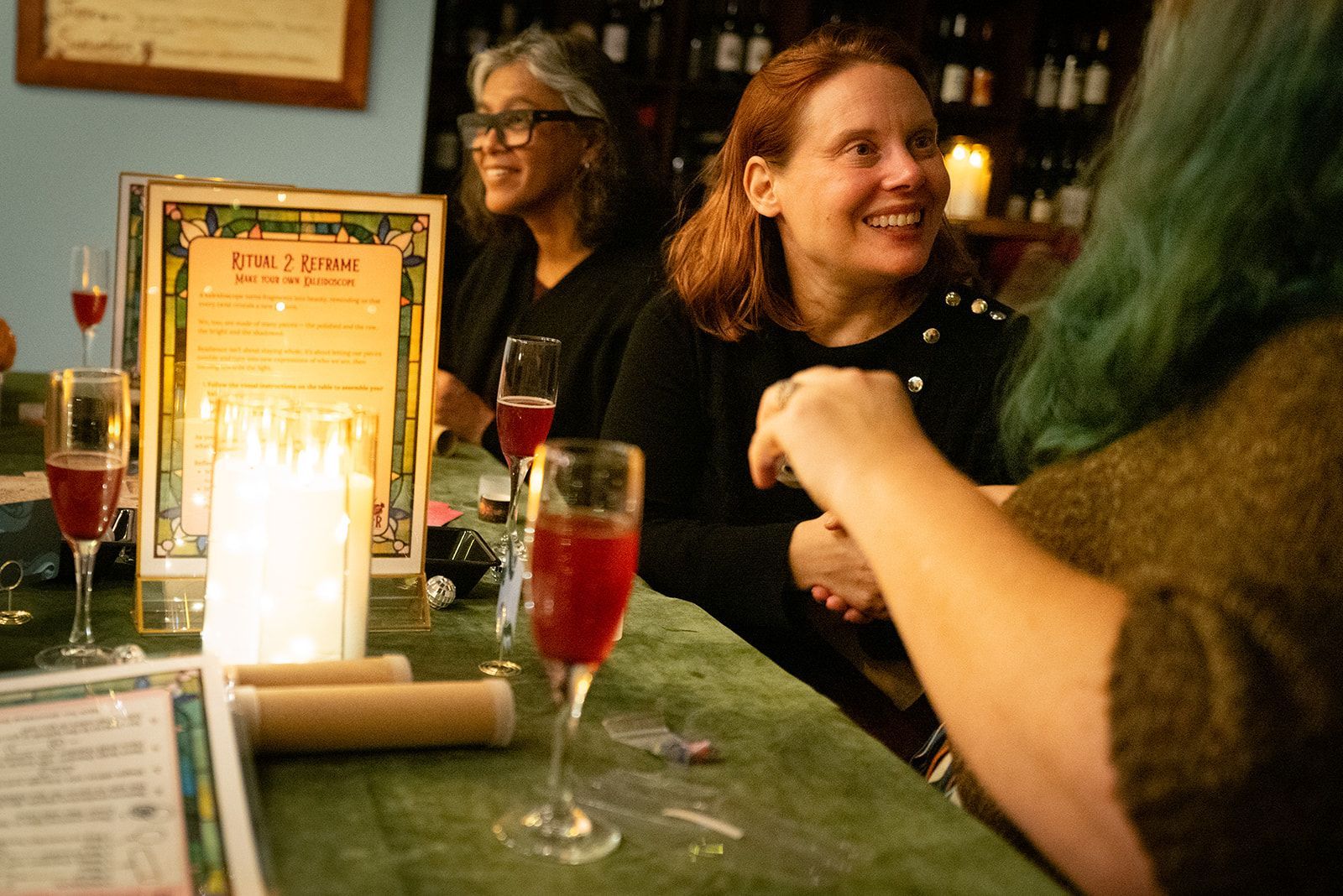 People chatting at a candlelit restaurant table with drinks and a menu display