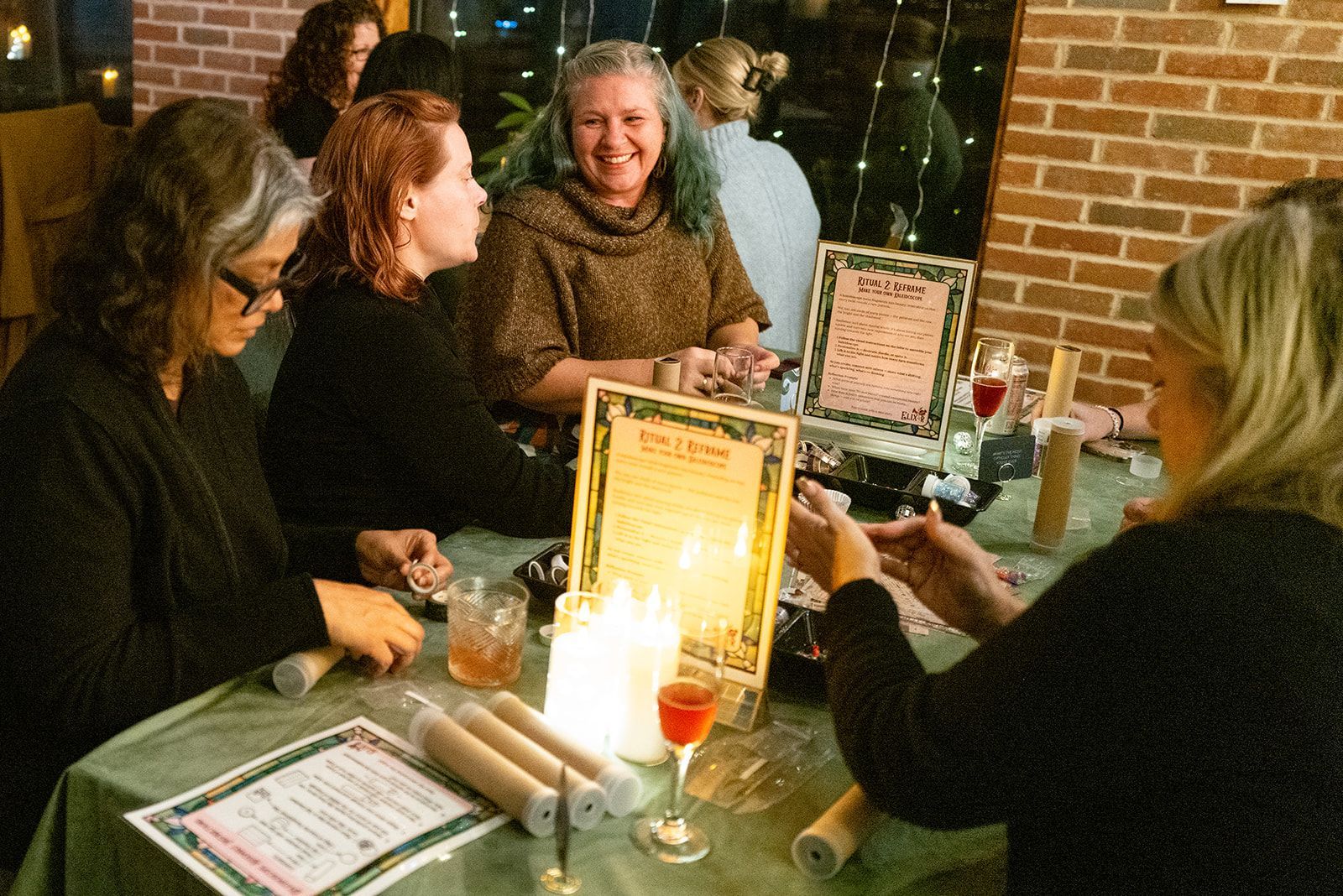 Four people chatting at a restaurant table with menus and drinks near a brick wall